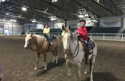 Two riders on horseback in an indoor arena.